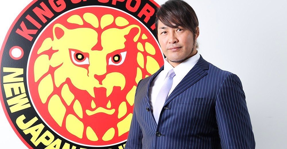 Hiroshi Tanahashi in a pin-striped suit standing in front of the NJPW Lion's Mark logo as the President of NJPW.